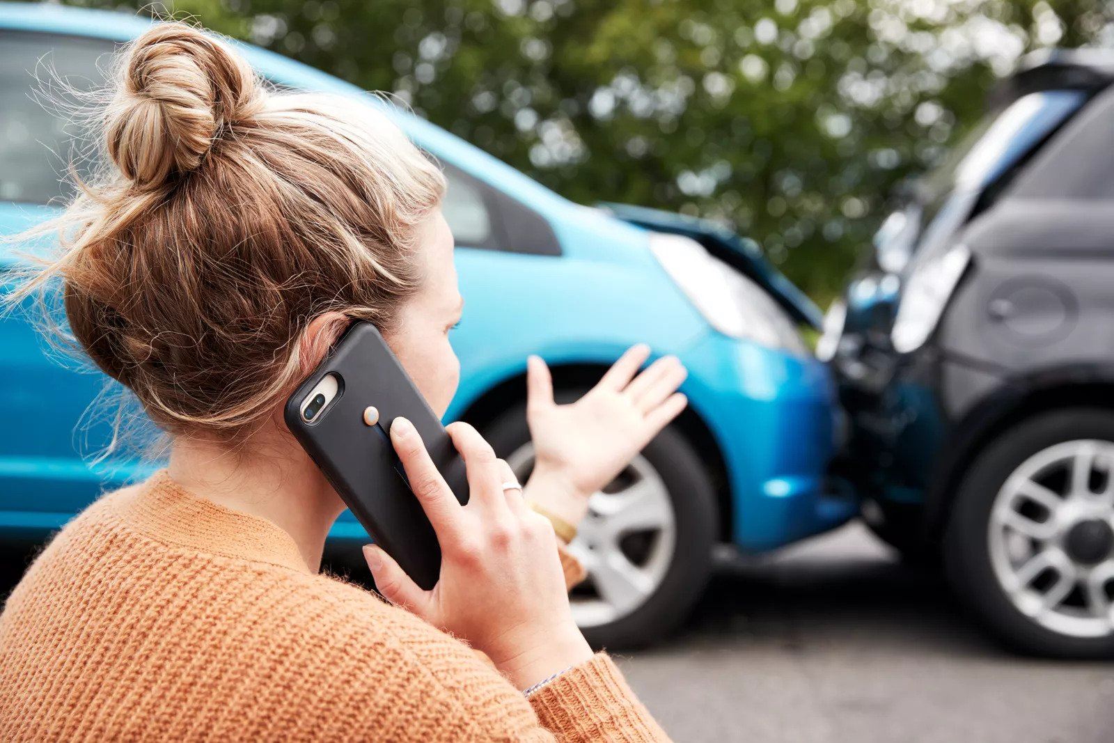 girl sitting on the curb talking on her phone after car accident